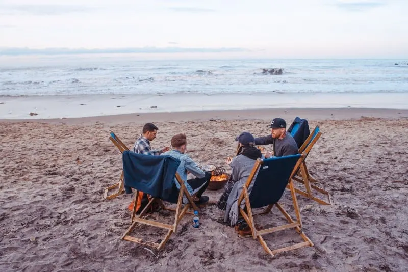 three men and one woman sitting on beach lounge near bonfire