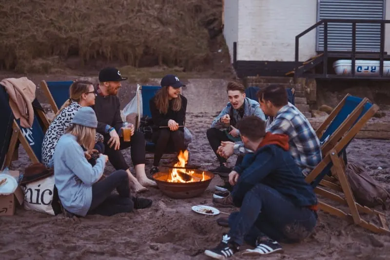 group of people sitting by bonfire at beach