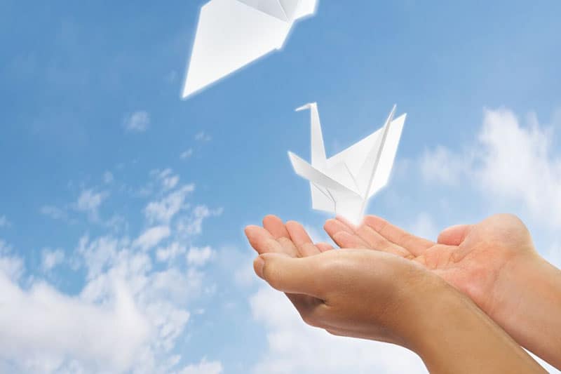 person hands letting go of an origami made bird flying