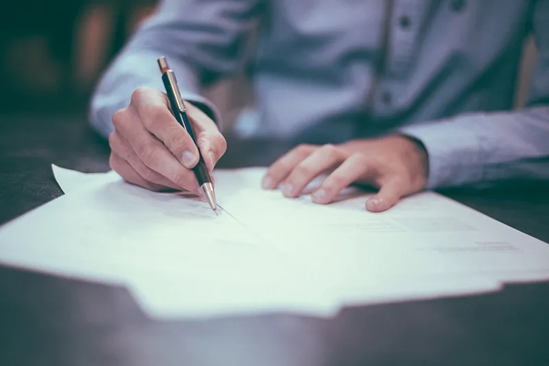 person holding a pen while writing on white paper