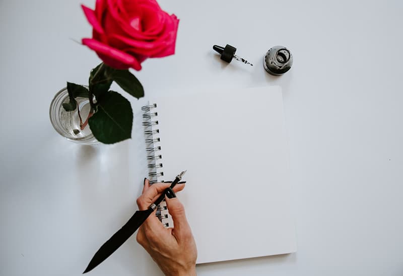 pessoa com caneta preta a escrever num caderno branco