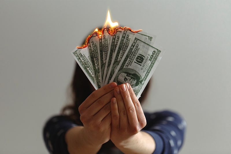 person holding fake us dollars on fire