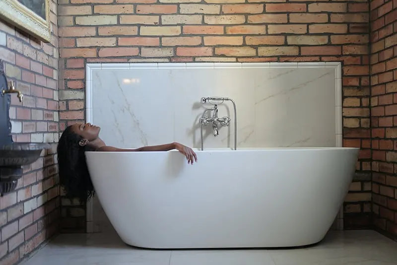 person in a bathtub near brick wall