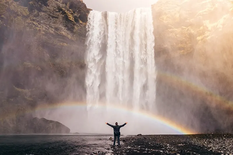person in front of waterfalls with double rainbow