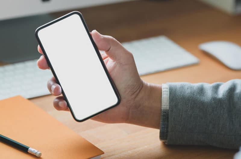 persona apoyada en mesa de madera con teléfono en la mano con pantalla en blanco