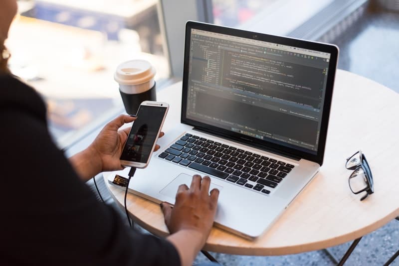 person looking at phone connected to the macbook pro placed at the table