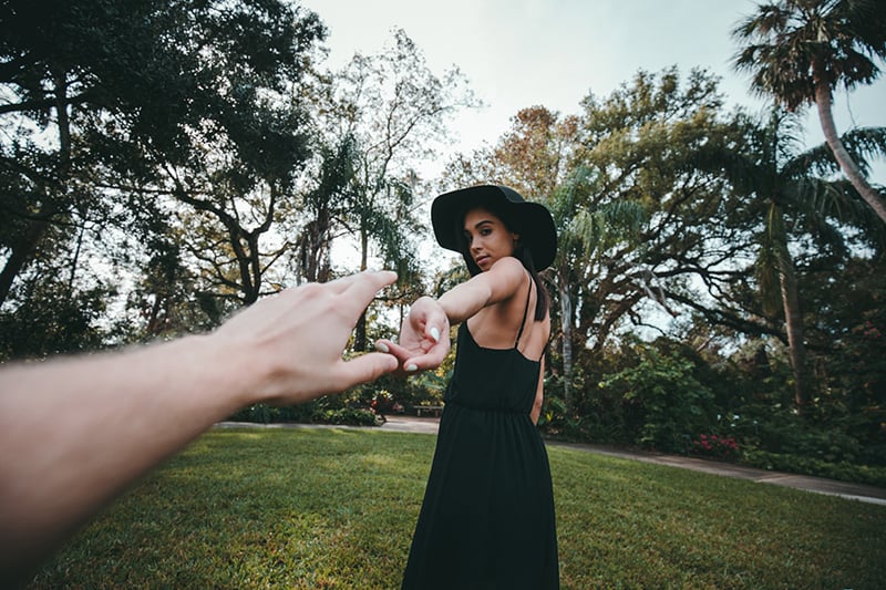 person reaching woman's hand while standing on green grass