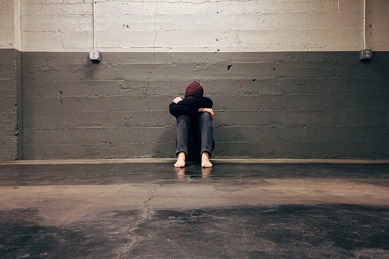 person sitting alone on the floor near concrete wall