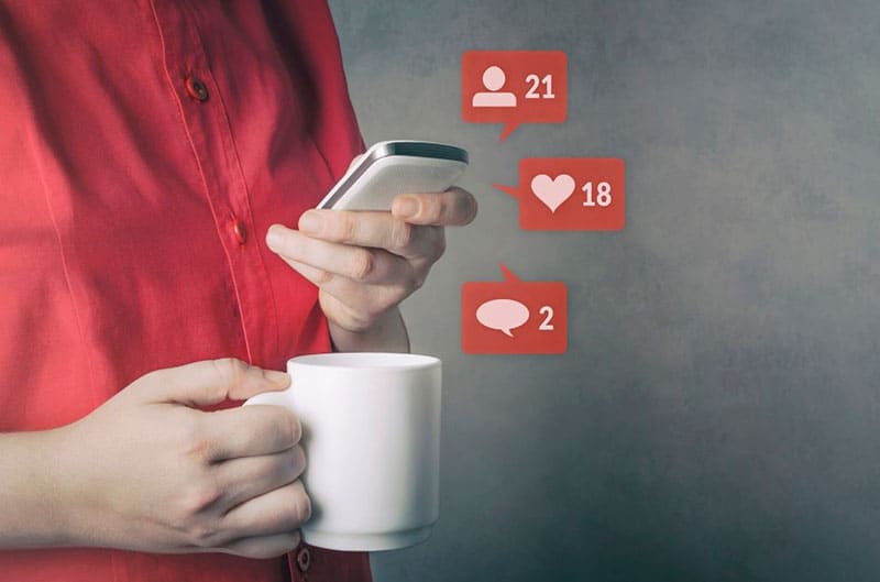 person using social media bringing mug and cellphone with like heart chat icons