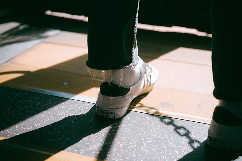 persona che indossa scarpe da ginnastica basse bianche in piedi su un pavimento di legno marrone 