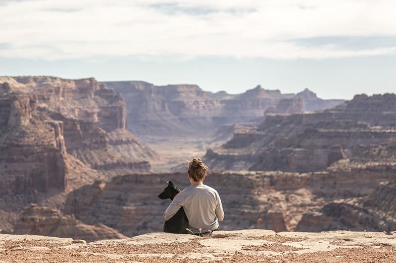 persona con cane seduta sulla scogliera del Grand Canyon