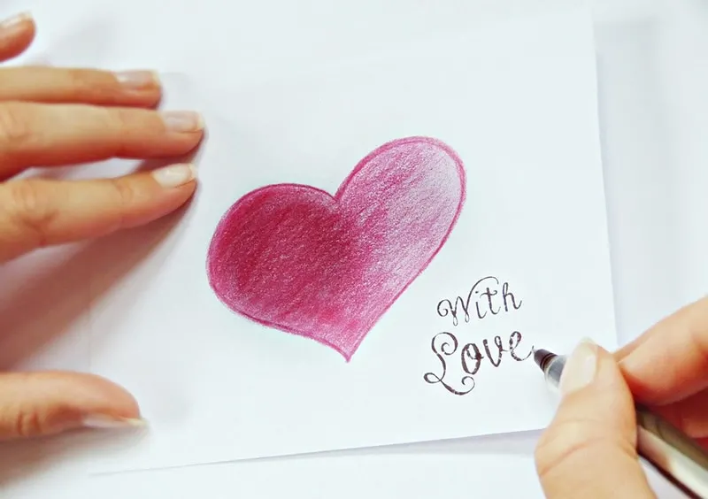 person writing a note beside drawing of heart
