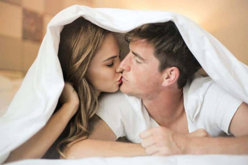 foto di coppia che si bacia sotto le lenzuola