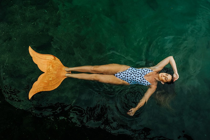 foto di una donna che galleggia su uno specchio d'acqua con le pinne a coda di sirena