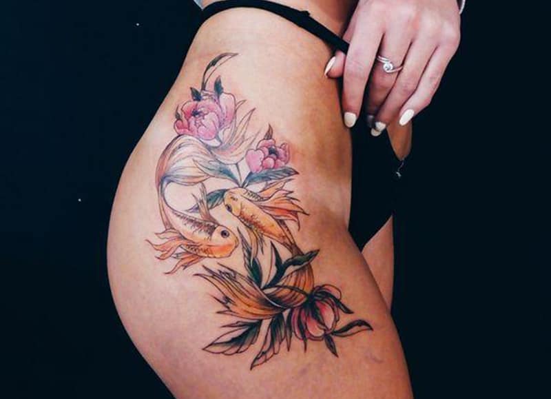 pisces tattoo on the thigh surrounded with flowers