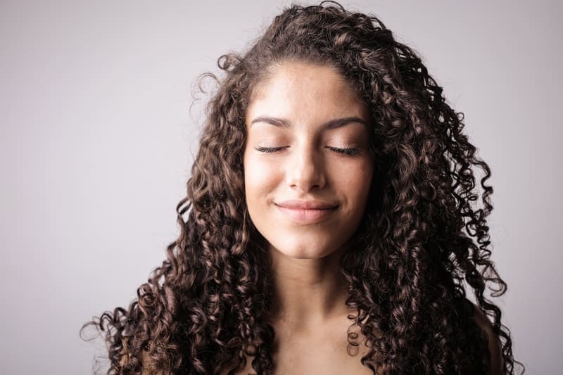 portrait photo of smiling woman with curly hair while closing her eyes