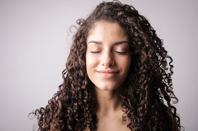 foto ritratto di donna sorridente con capelli ricci mentre chiude gli occhi