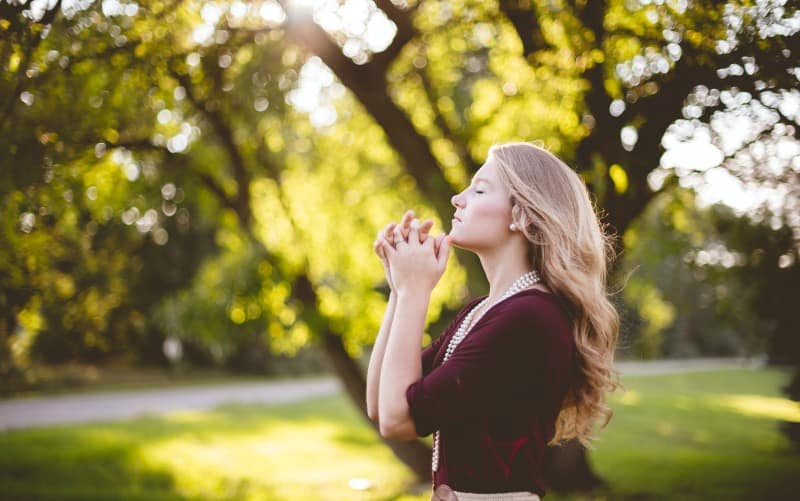 Giovane donna bionda in preghiera nel parco durante il giorno