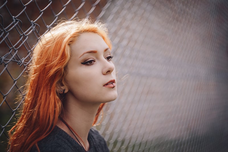 red hair woman leaning on gray fence