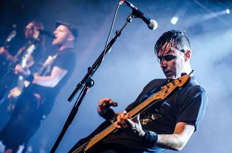 rocker gut strumming a guitar in the stage and other team rock members
