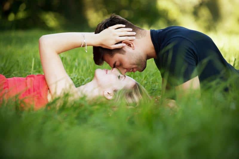 Coppia romantica nella natura che si bacia sdraiata sull'erba