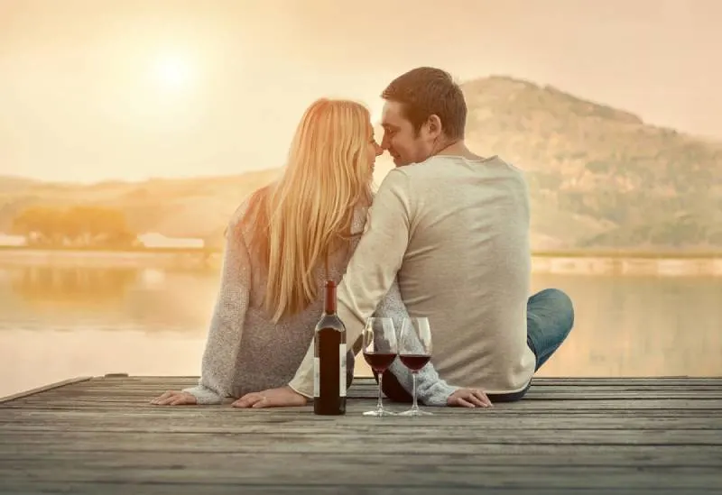romantic couple sitting in front of lake on sunset