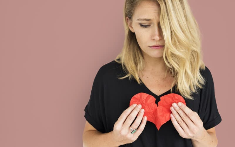 Sad blonde woman in black top holding broken red paper heart