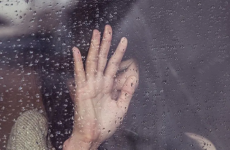 sad woman leaning on the glass hand covering her face