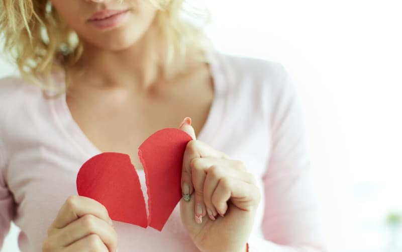 Primer plano de mujer triste mostrando corazón rojo de papel roto