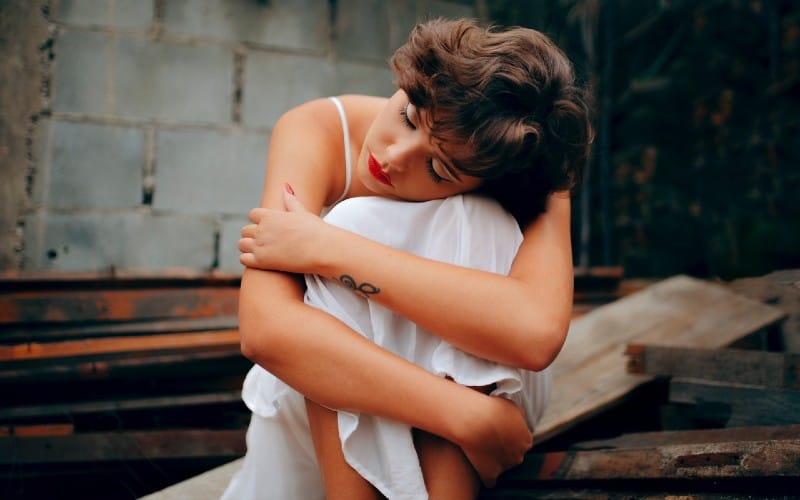 Mujer triste sentada con la cabeza sobre las rodillas cerca de un muro de hormigón gris