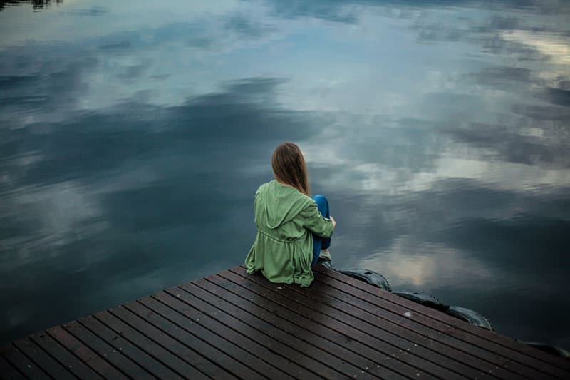 donna triste seduta in riva al lago