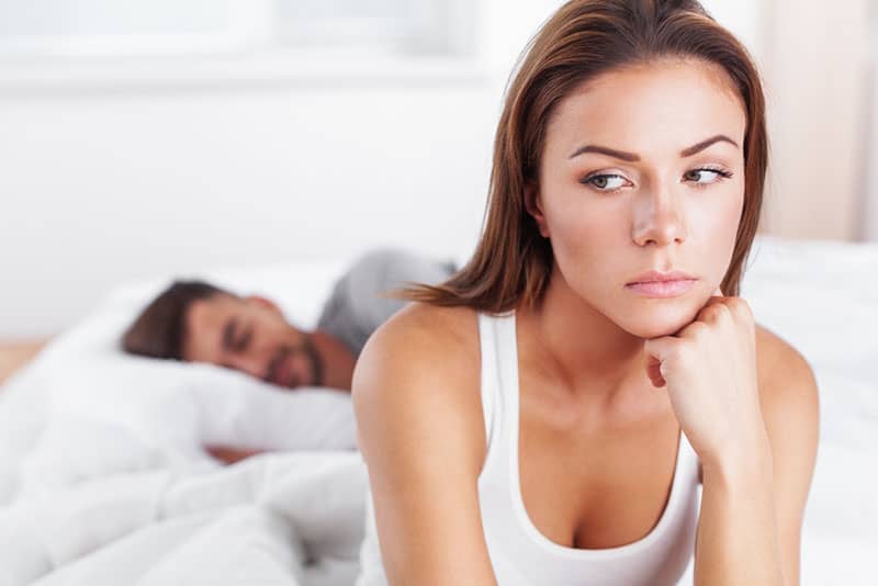 donna triste seduta sul letto mentre l'uomo dorme