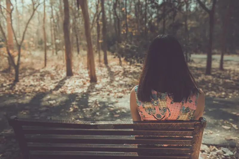 sad woman sitting on the bench in the wood
