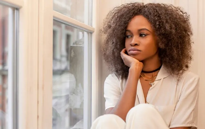 Sad woman sitting on the window during daytime