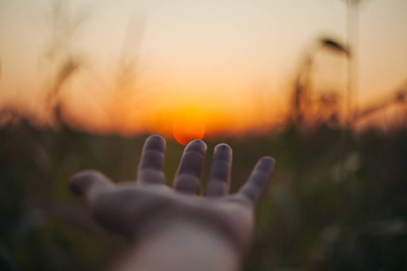 Foto con messa a fuoco selettiva di una persona che posa la mano sul tramonto