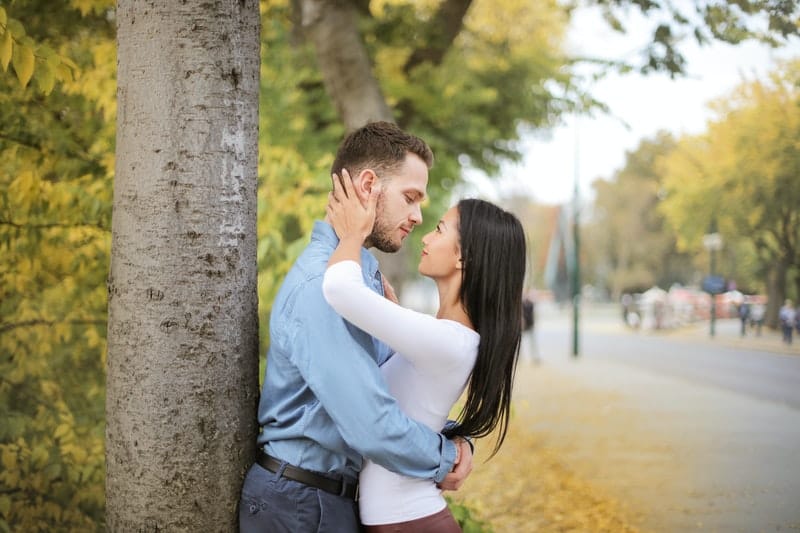 selective photo of a couple embracing and seeing eye to eye by a tree 