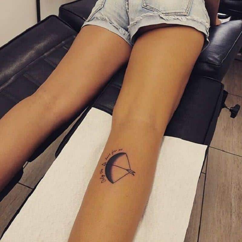 tatuagem de arco e flecha sombreada combinada com citação na perna de uma mulher