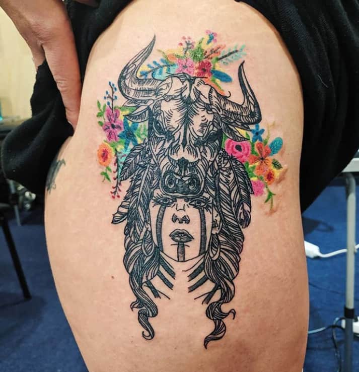 Tatuagem de uma rapariga xamã com um touro na cabeça rodeada de flores