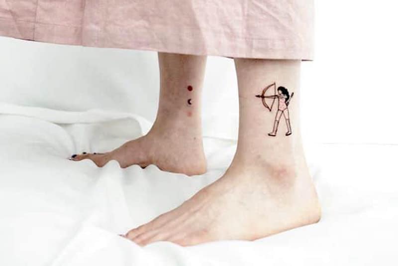 tatuagem "shooting for the stars" com stagittarius num tornozelo e estrelas no outro tornozelo