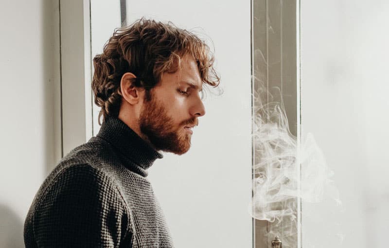 foto lateral de un hombre con top de cuello de tortuga y humo de cigarro