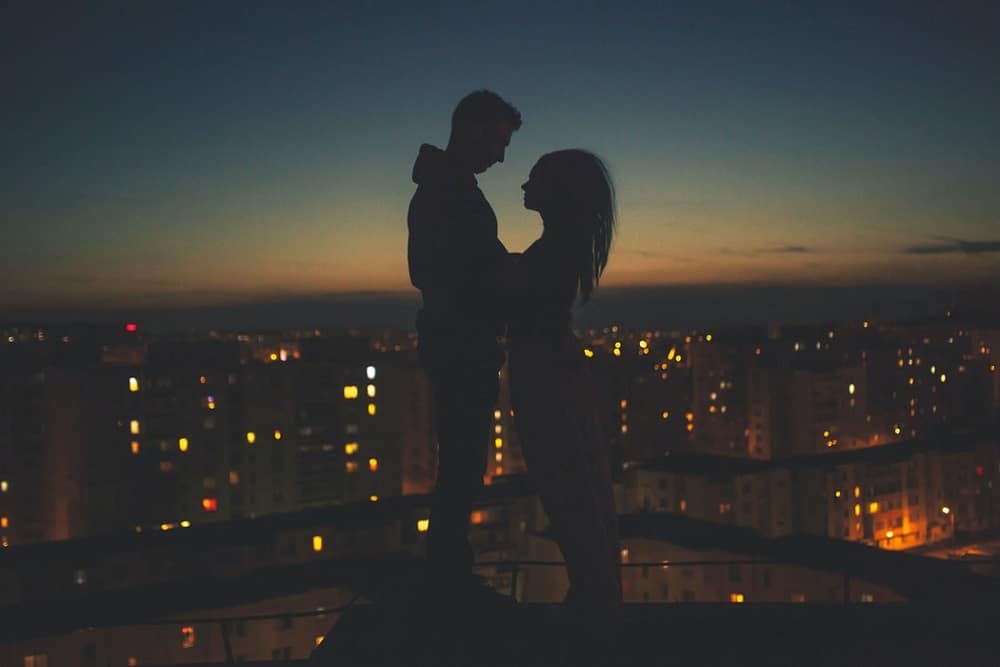 silhouette of ma and woman standing on roof building at night