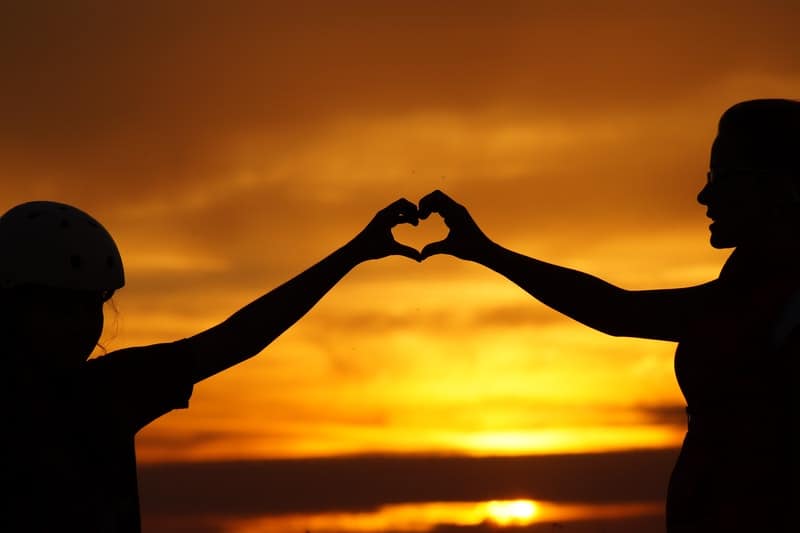 silhouette of man touching a woman in sunset forming heart shape