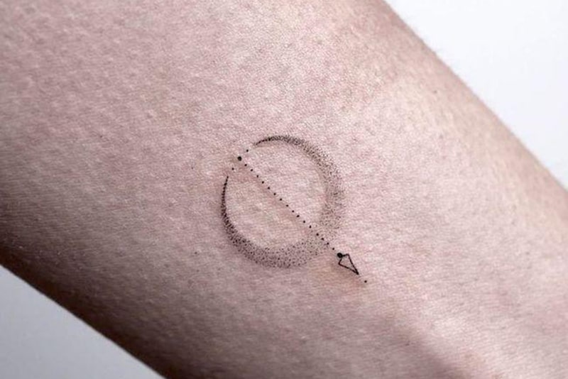 tatuagem de uma pequena seta rodeada por uma lua no pulso