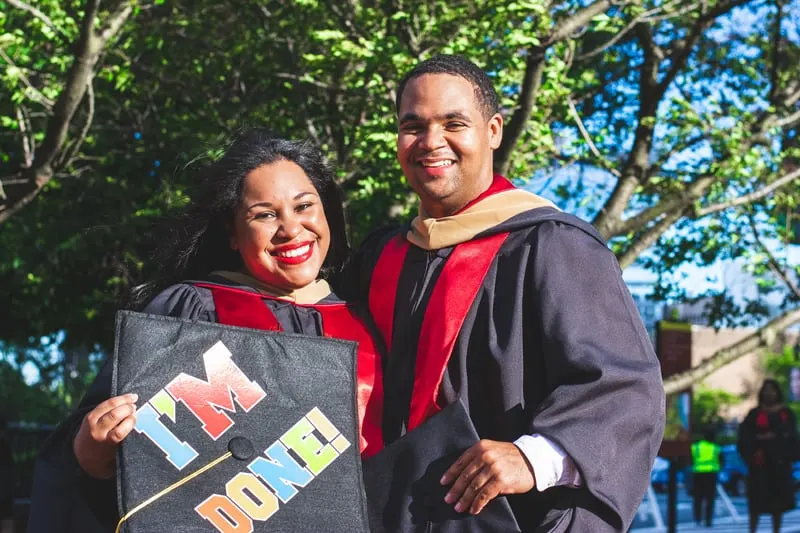 smiling man and woman in graduation toga with woman carrying Im Done signage