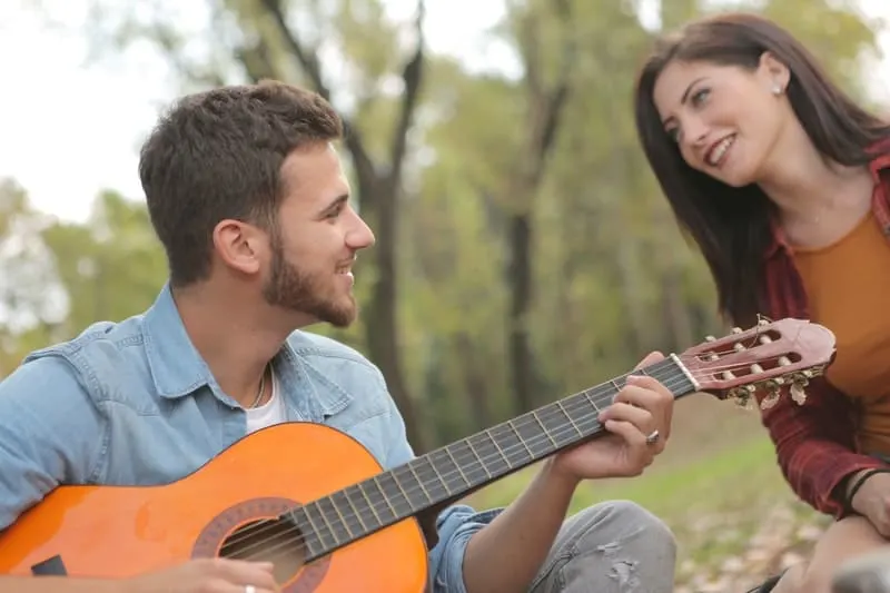 smiling man playing guitar beside a happy woman in the park