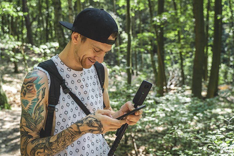 uomo sorridente con zaino in mano smartphone nel bosco
