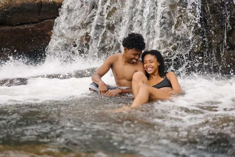 smiling topless man sitting near his girlfriend near waterfall