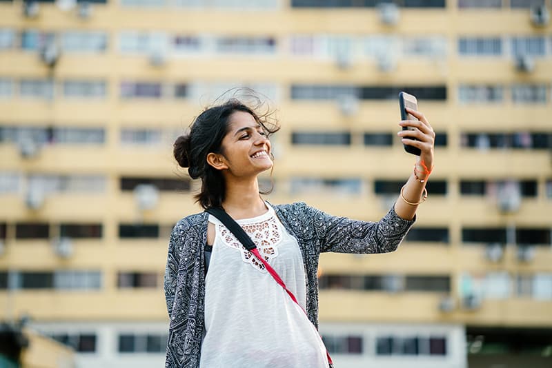 mujer sonriente sosteniendo un smartphone negro mientras se toma un selfie