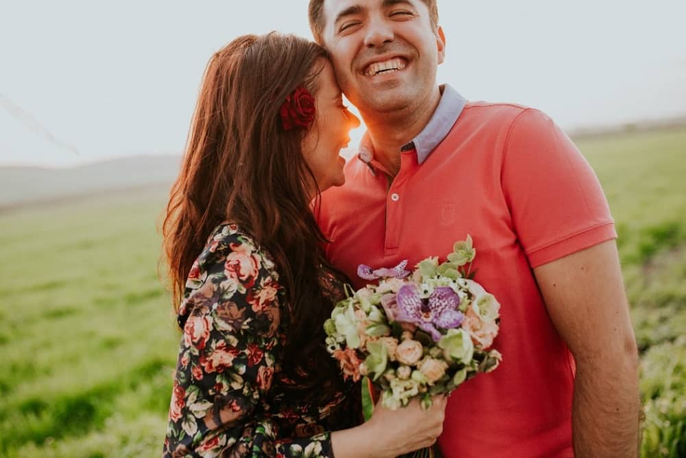 smiling woman hugging smiling man holding flowers