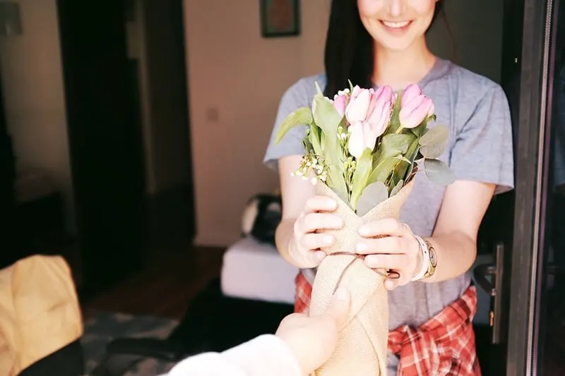 smiling woman receiving flower bouqet from man